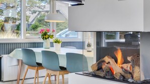 Ein moderner Essbereich mit Kamin, Tisch und Stühlen sowie Blick ins Freie.