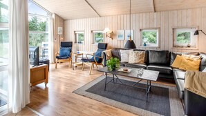 A spacious living room with wooden walls and ceiling, a black leather sofa, a wooden coffee table, and a large window offering a view of greenery outside. - "Ronna" - 2.2km from the sea by Interhome (Blåvand)