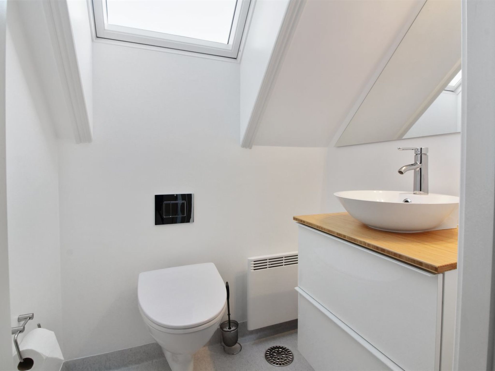 A modern bathroom with a skylight, a white toilet, a wooden vanity with a white sink, and a toilet paper holder.
