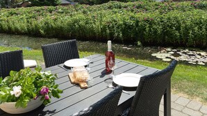 An outdoor dining table with wicker chairs, a bottle of red wine, and a loaf of bread on a sunny day. - "Moa" - 800m from the sea by Interhome (Blåvand)