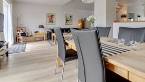 A modern living room with a dining area, featuring a wooden dining table, grey upholstered chairs, a white pendant light, and a minimalist decor style. - "Moa" - 800m from the sea by Interhome (Blåvand)