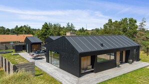 Une maison moderne, dotée d’un toit noir, d’une terrasse en bois et d’une porte vitrée donnant sur un espace patio.