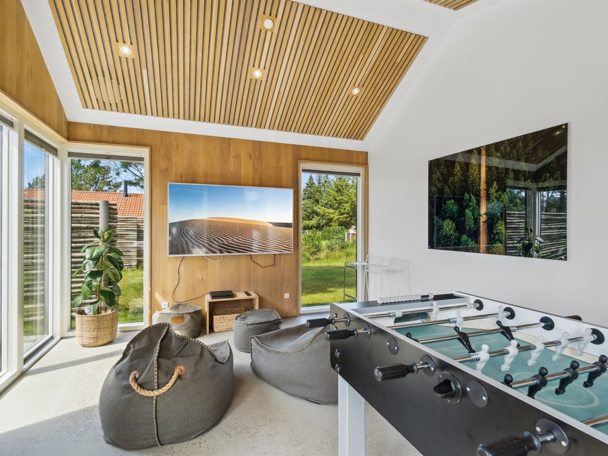 Una sala de estar moderna con una mesa de fútbol de mesa, un televisor grande y vistas a un jardín.