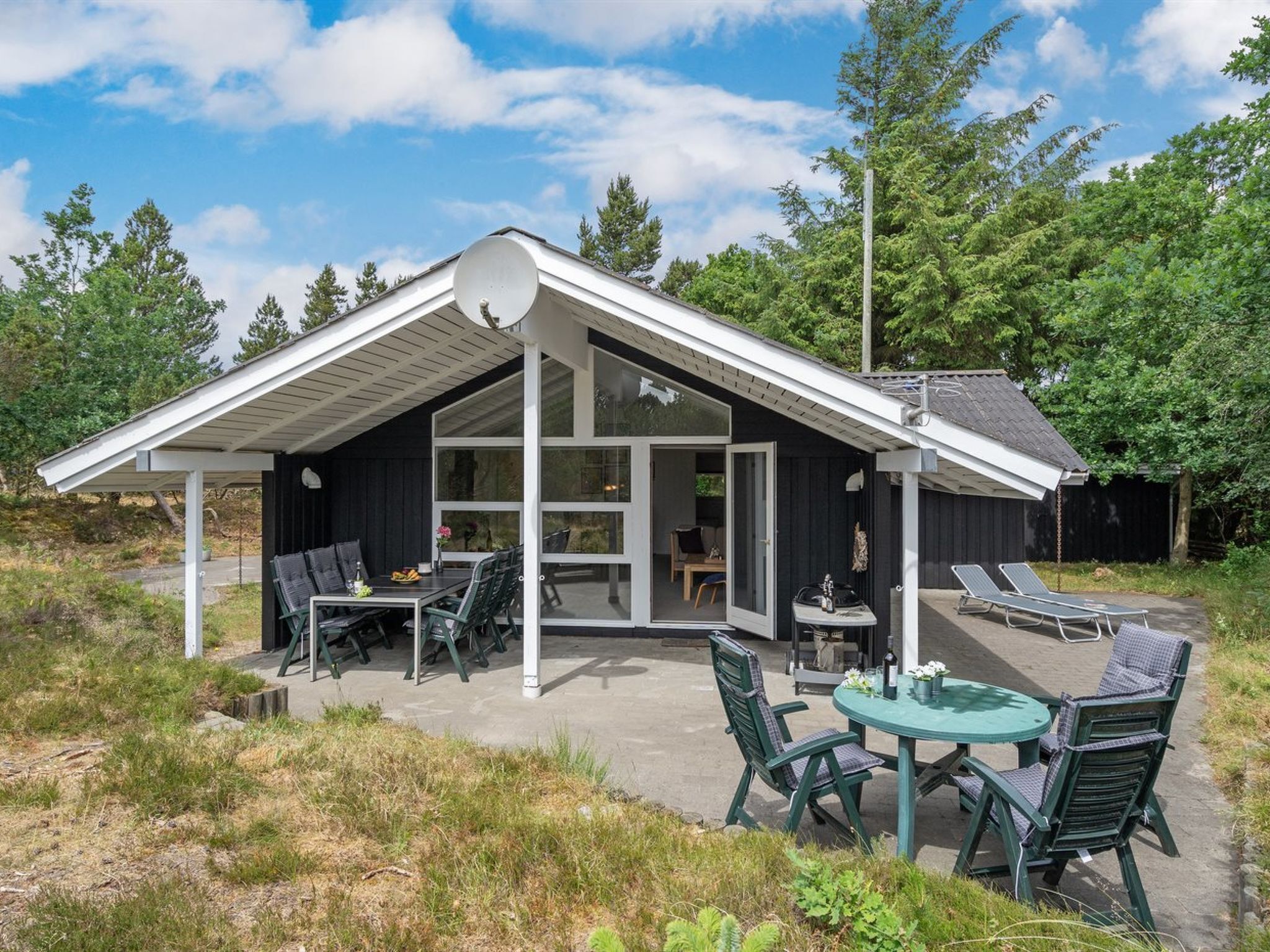 A modern house with a covered patio, outdoor seating, and a large window.