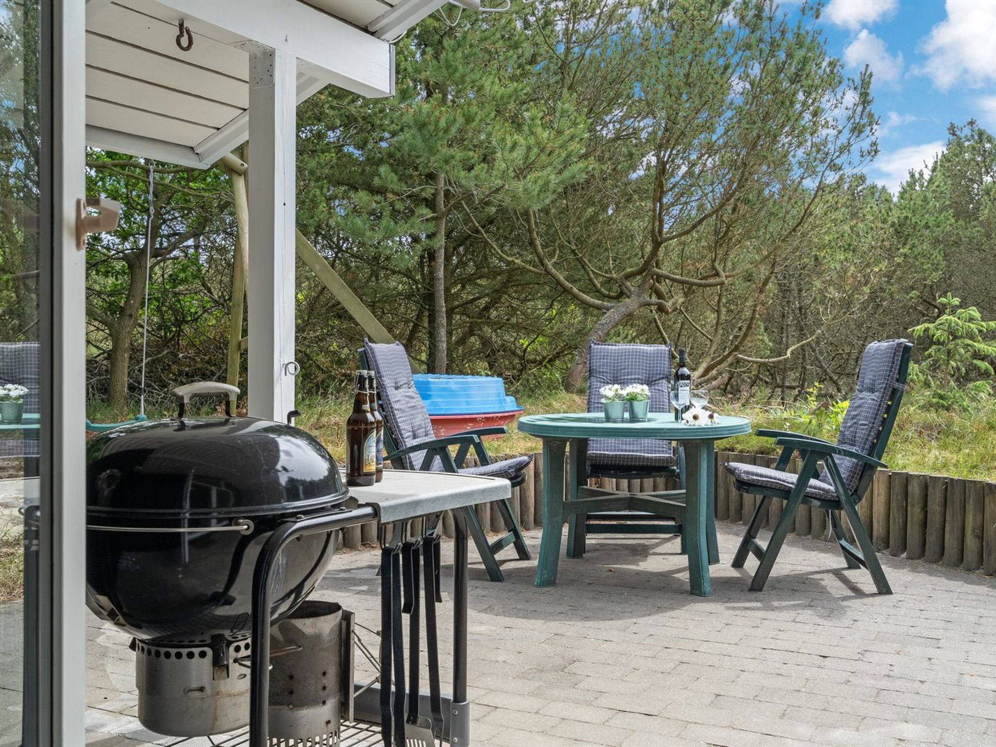 Een terras buiten met een barbecue, stoelen en een eettafel.