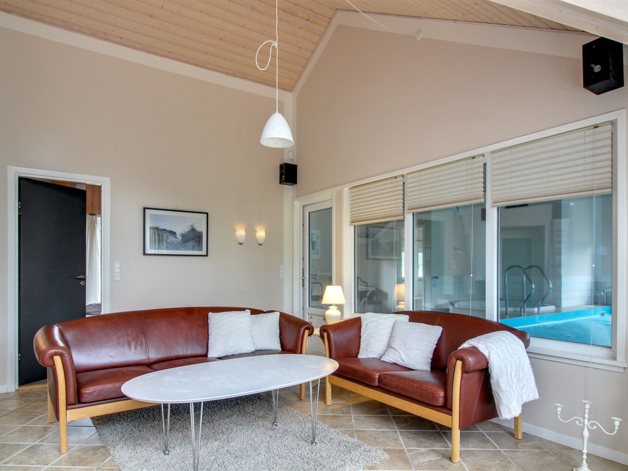 A modern living room with a brown leather sofa, a round coffee table, and a large window with a view of a swimming pool.