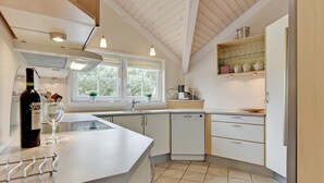 Una cocina moderna con una isla grande, armarios blancos y un lavavajillas integrado. Hay ventanas que ofrecen luz natural y vistas al exterior.