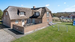 A large brick house with a thatched roof, a covered patio, and a small garden.