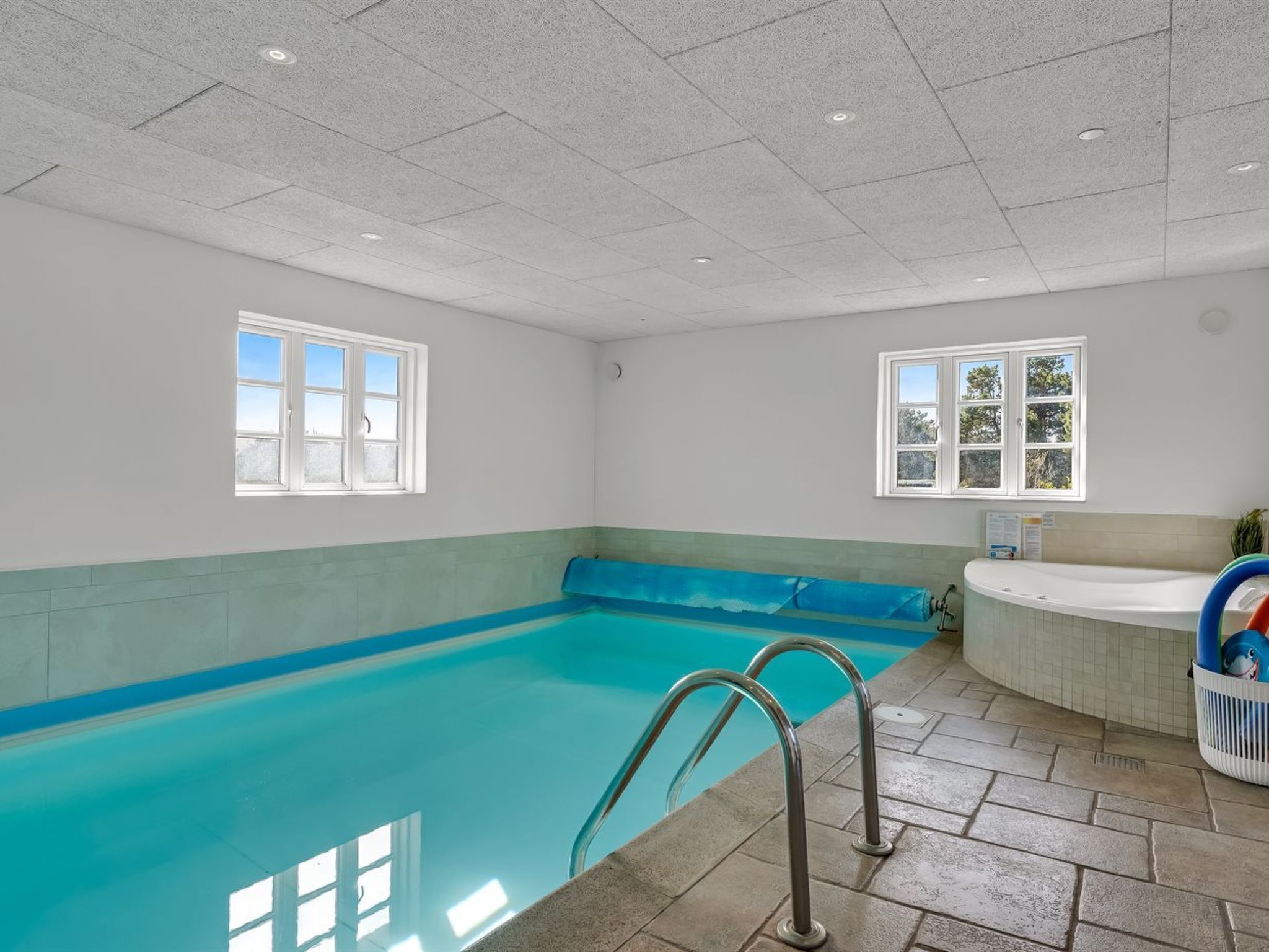 Una piscina interior con agua azul cristalina, un jacuzzi y suelo de baldosas.