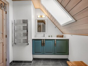 Une salle de bain moderne avec une douche à parois de verre, un meuble-lavabo blanc doté de placards turquoise et un puits de lumière.