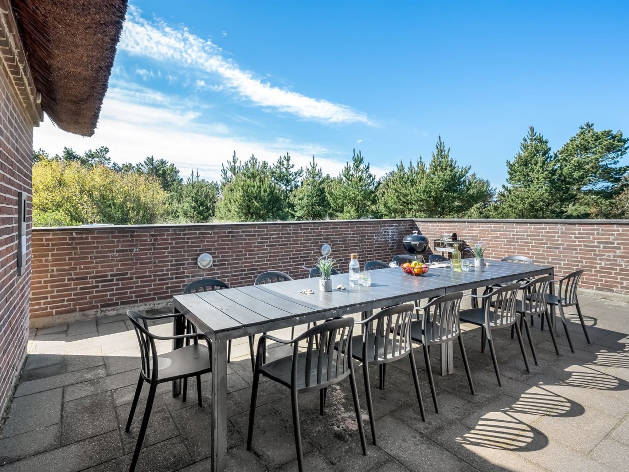 An outdoor patio with a brick wall, a long table, and chairs.