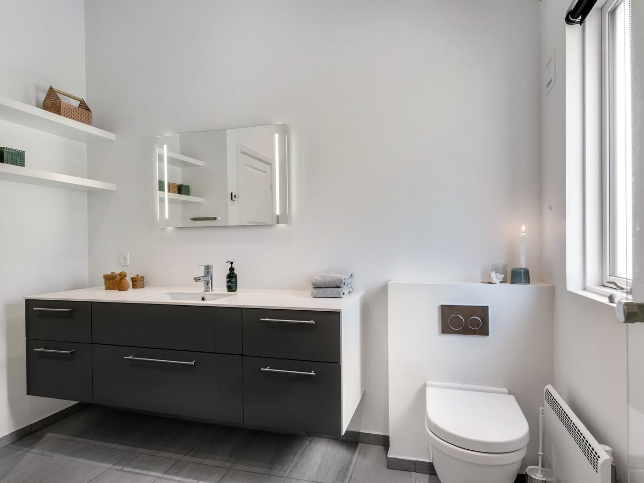 Un bagno moderno con un mobile lavabo bianco, armadietti scuri, un water bianco e una finestra con vista.