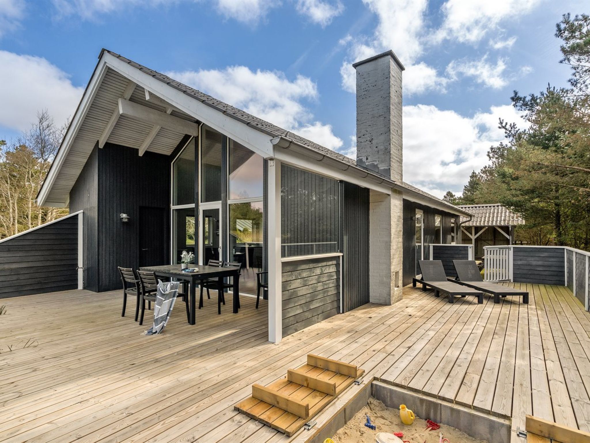 Une maison moderne dotée d’une grande terrasse, d’une cheminée et d’un coin repas aménagé avec du mobilier d’extérieur.