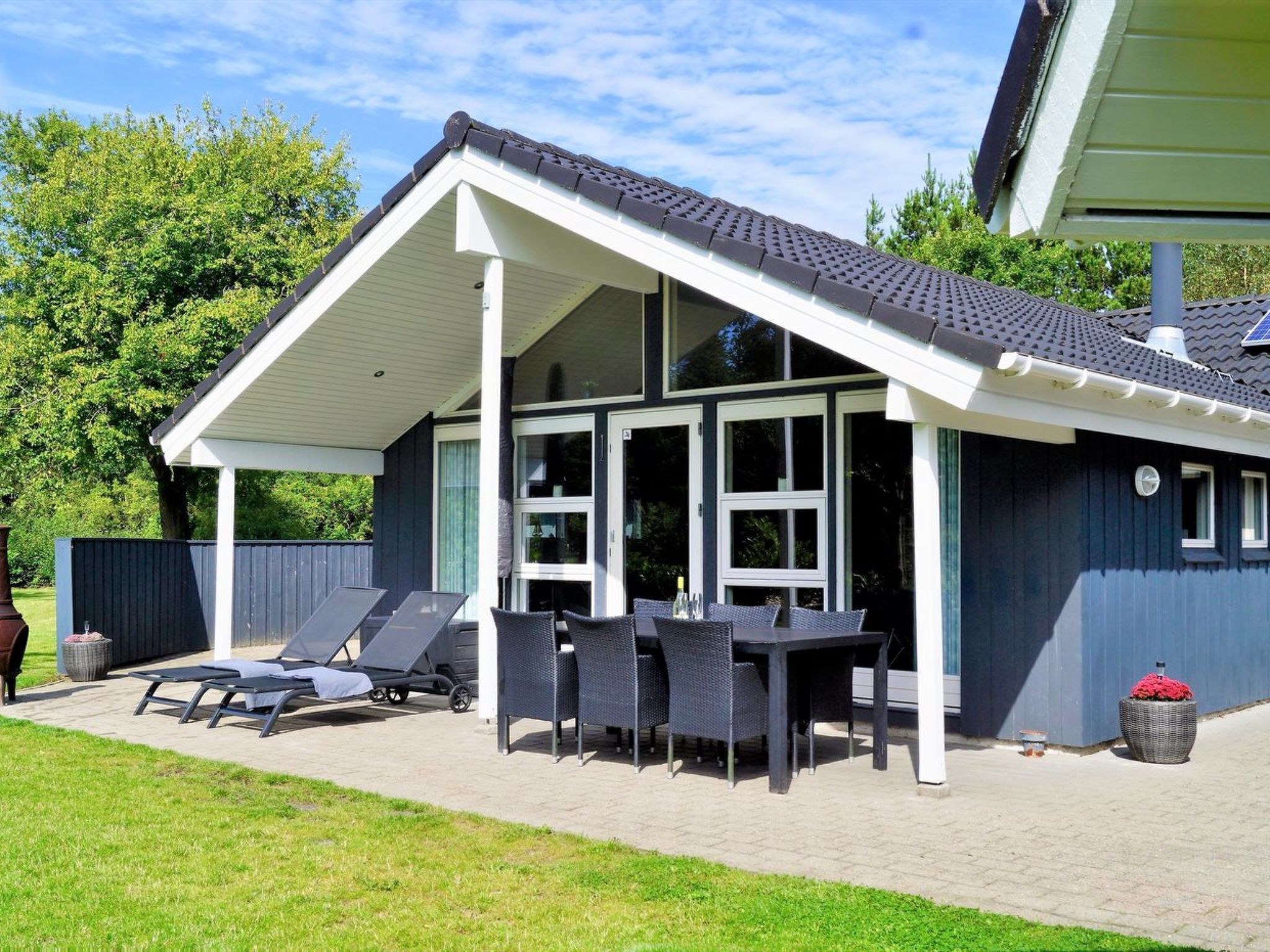 Un patio extérieur couvert, équipé d’une table et de chaises, d’un barbecue et d’un espace délimité par une clôture.