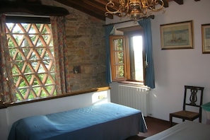 A bedroom with a bed, a window with curtains, a radiator, and a chair.