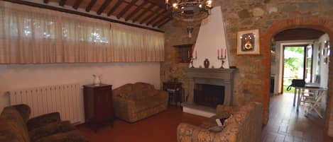 A traditional living room with a fireplace, wooden beams, and a stone wall.