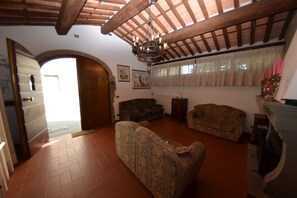 A living room with a fireplace, two sofas, a wooden ceiling, and a door leading to another room.
