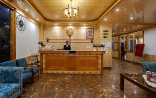 A lobby with a wooden reception desk, a clock, and a receptionist.