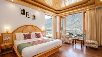 A spacious bedroom with a large bed, wooden headboard, and a balcony with a mountain view.