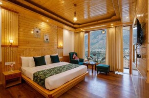 A wooden-paneled bedroom with a bed, a chair, a small table, and a balcony with a view of the mountains.