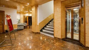 A lobby with a marble floor, wooden walls, a staircase, and a glass elevator. - Mnp Village Venue (Manali)