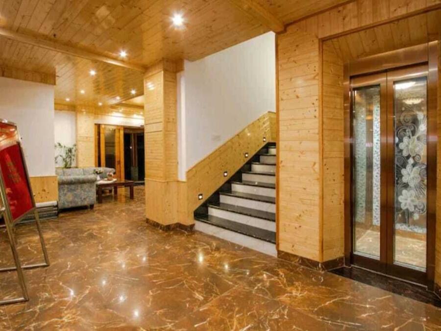 Un hall d’entrée avec un sol en marbre, des murs en bois, un escalier et un ascenseur en verre.