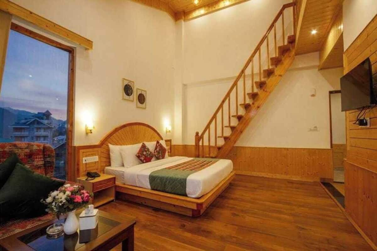 A bedroom with a wooden bed, a nightstand, a dresser, a wooden staircase, and a large window with a view of buildings.