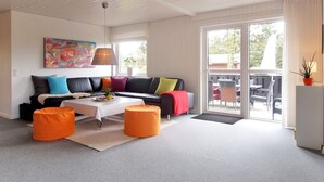 Ein modernes Wohnzimmer mit einem schwarzen Ledersofa, bunten Kissen, einem weißen Couchtisch und orangefarbenen Poufs.
