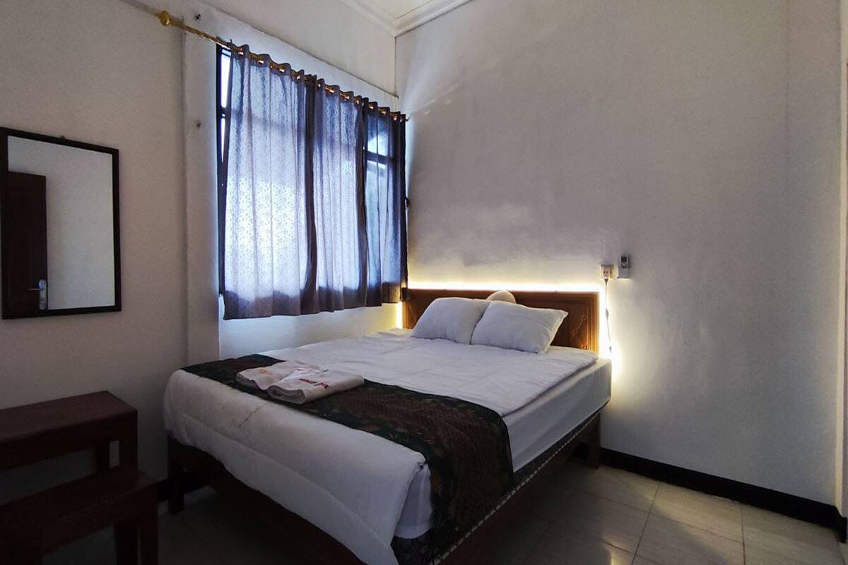 Una cama bien hecha con cabecera, mesita de noche y ventana con cortinas.