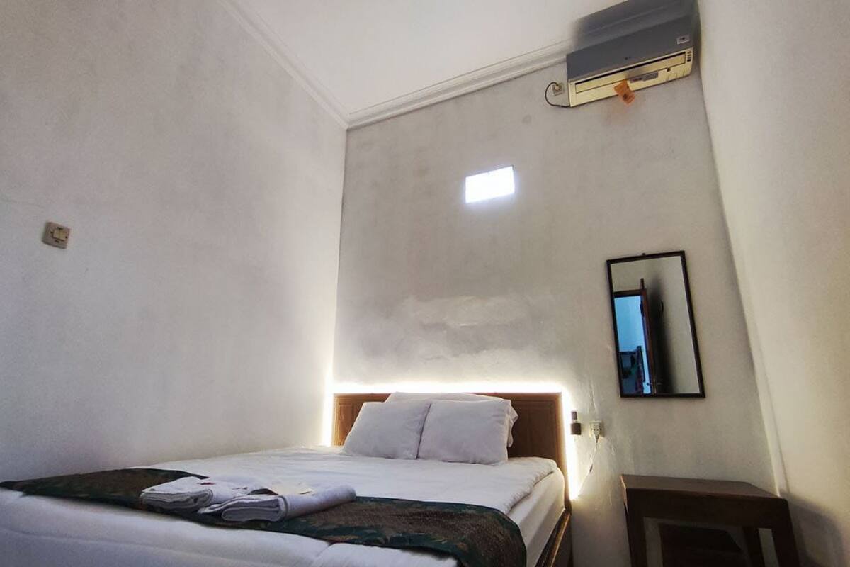 Habitación de hotel con cama, una mesita de noche, aire acondicionado instalado en la pared y una ventana con luz natural.
