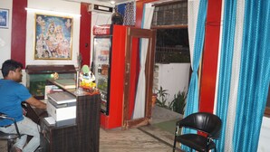 Quarto com escrivaninha, frigorífico, cadeira e janela com cortinas.