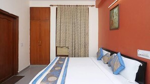 Quarto de hotel com cama, guarda-roupa de madeira, cortina e luminária fixada na parede.