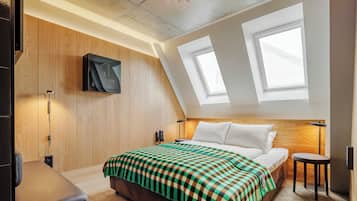Una camera d'albergo moderna con soffitto a falde, pareti rivestite in legno, un grande letto con coperta a scacchi, una scrivania e una TV a parete.