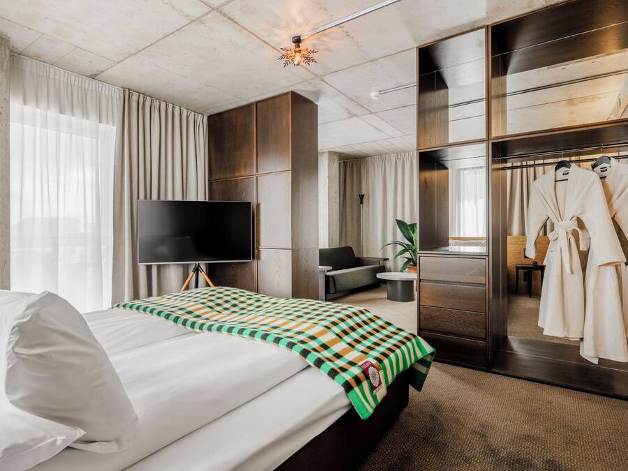 A hotel room with a bed, a TV, a seating area, and a mirror with robes.