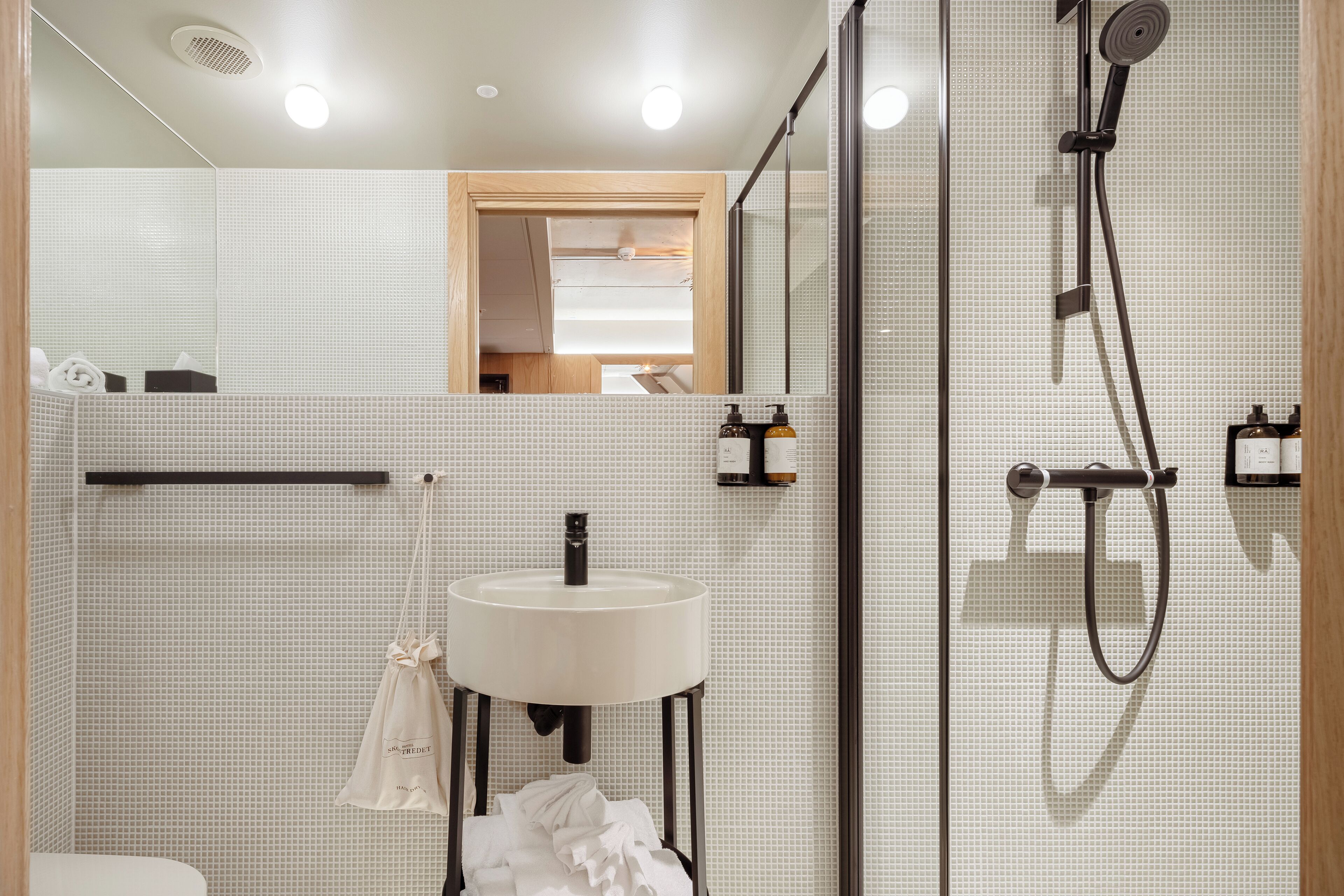 A modern bathroom with a white sink, a handheld showerhead, and a towel rack.