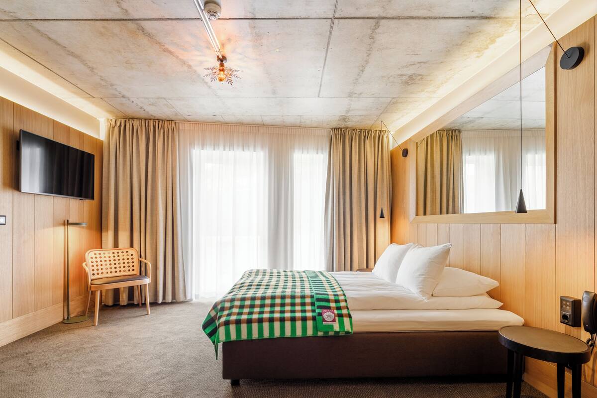 A hotel room with a large bed, a flat-screen TV mounted on the wall, a chair, and a small table.
