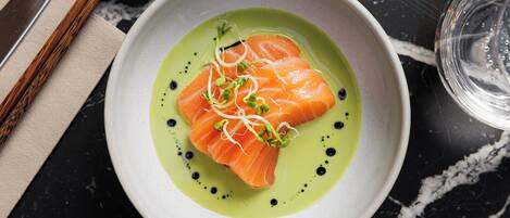 A bowl of food with a green sauce, garnished with sprouts and black dots.