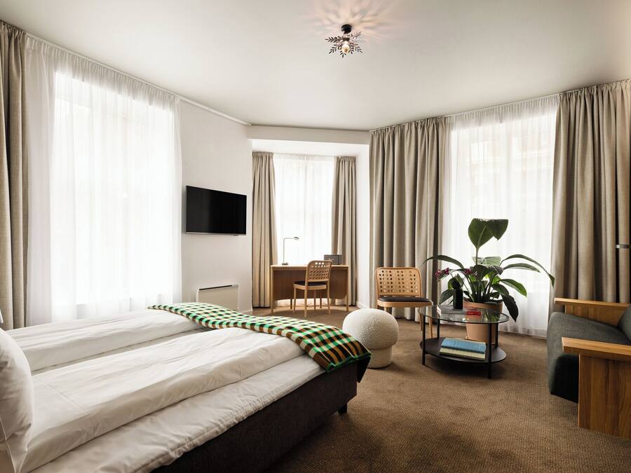Een hotelkamer met een bed, een bureau, een stoel, een televisie en een kamerplant.
