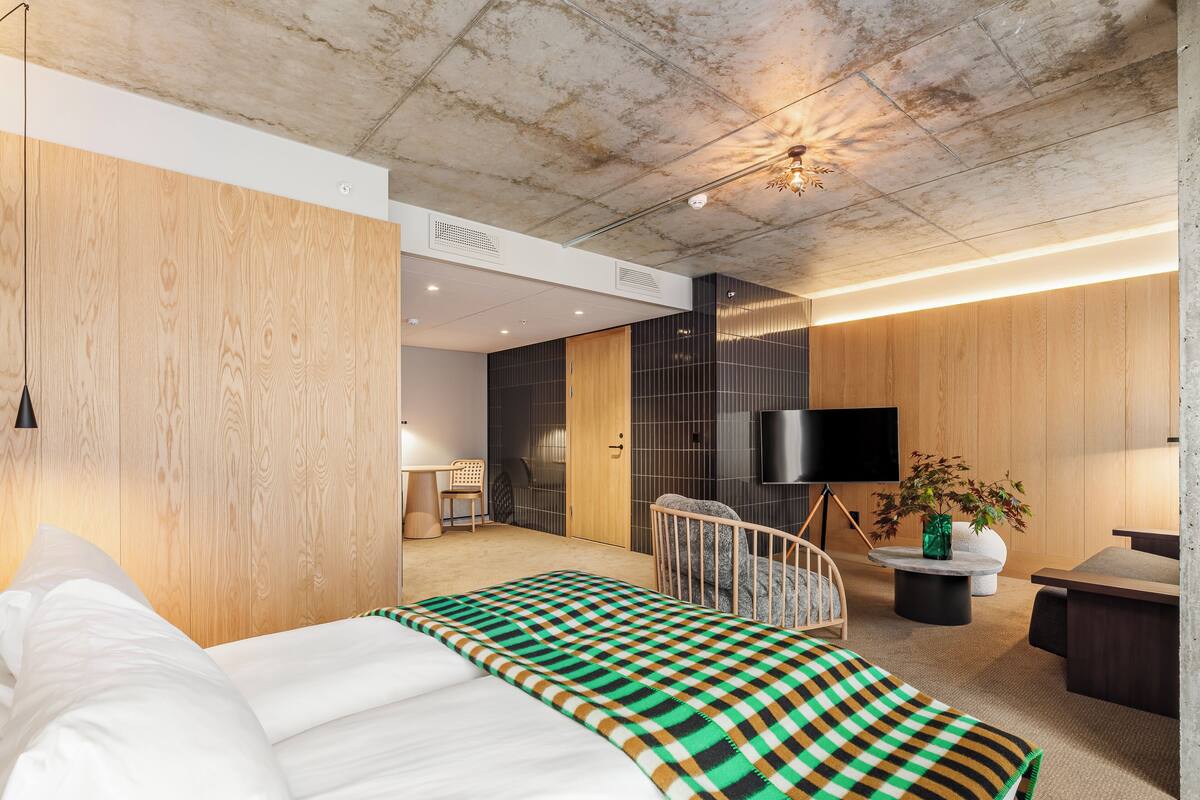 A modern hotel room with a large bed, a desk, a chair, a TV, and a plant.