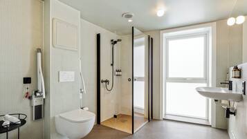 Un baño moderno con ducha envuelta en vidrio, inodoro blanco y lavamanos con espejo.