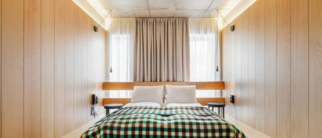 A hotel room with a large bed, wooden walls, a ceiling light, a bedside table, and a telephone.