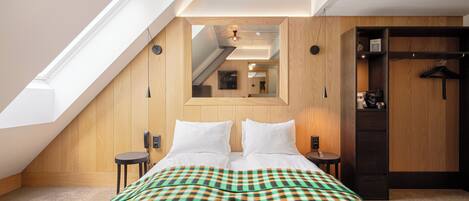 Un dormitorio con techo inclinado, una cama con manta a cuadros, un armario de madera y un espejo en la pared.