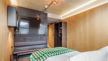 Quarto de hotel moderno com parede de madeira, um banco, uma cama com manta xadrez e luminária no teto.