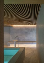Un baño moderno con pared de mármol, techo de listones de madera y bañera empotrada.