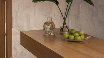 A marble-tiled floor, a wooden bench, a clear vase with a plant, and a bowl of green apples.