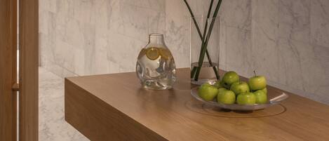 A marble-tiled floor, a wooden bench, a clear vase with a plant, and a bowl of green apples.