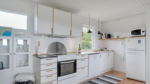 A modern kitchen with white cabinetry, a built-in oven, and a microwave. There is a wooden floor and a striped rug. - "Francis" - 300m from the sea by Interhome (Rødvig Stevns)