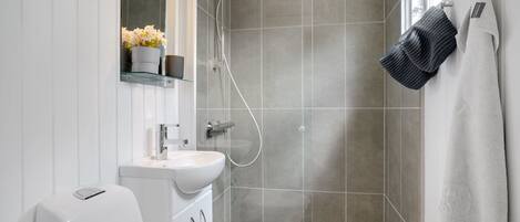 Un baño moderno con cabina de ducha de vidrio, un lavabo blanco y un perchero con toallas.