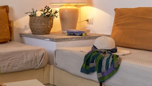 Une chambre d’hôtel bien rangée, avec un lit, une table de chevet dotée d’une lampe, une petite plante en pot et une pile de livres.