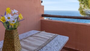 Un balcon orné d’un vase tressé rempli de fleurs, d’un tissu à rayures et offrant une vue sur la mer.